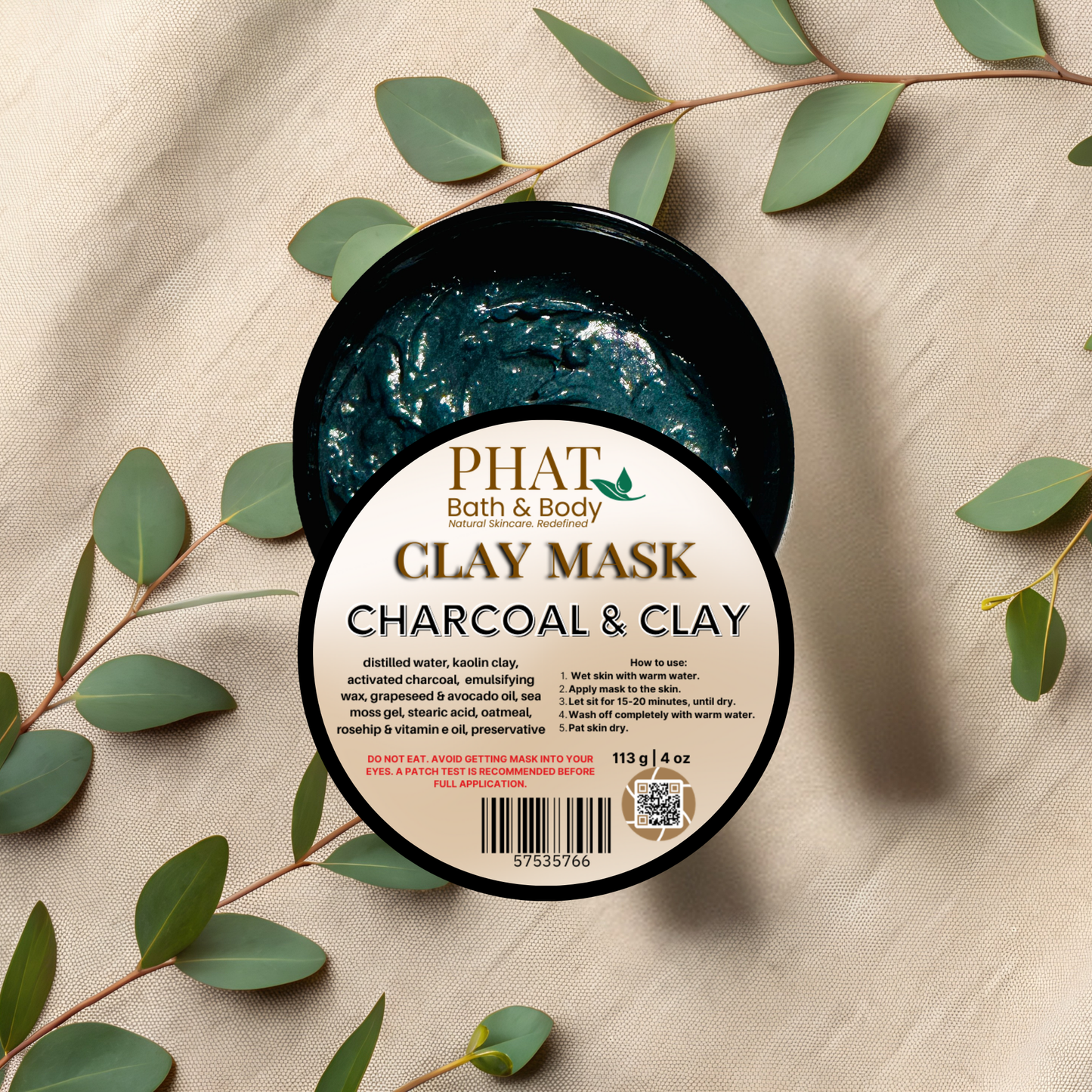 Jar of Phat Bath & Body Charcoal & Clay Mask with green leaves on a beige fabric background