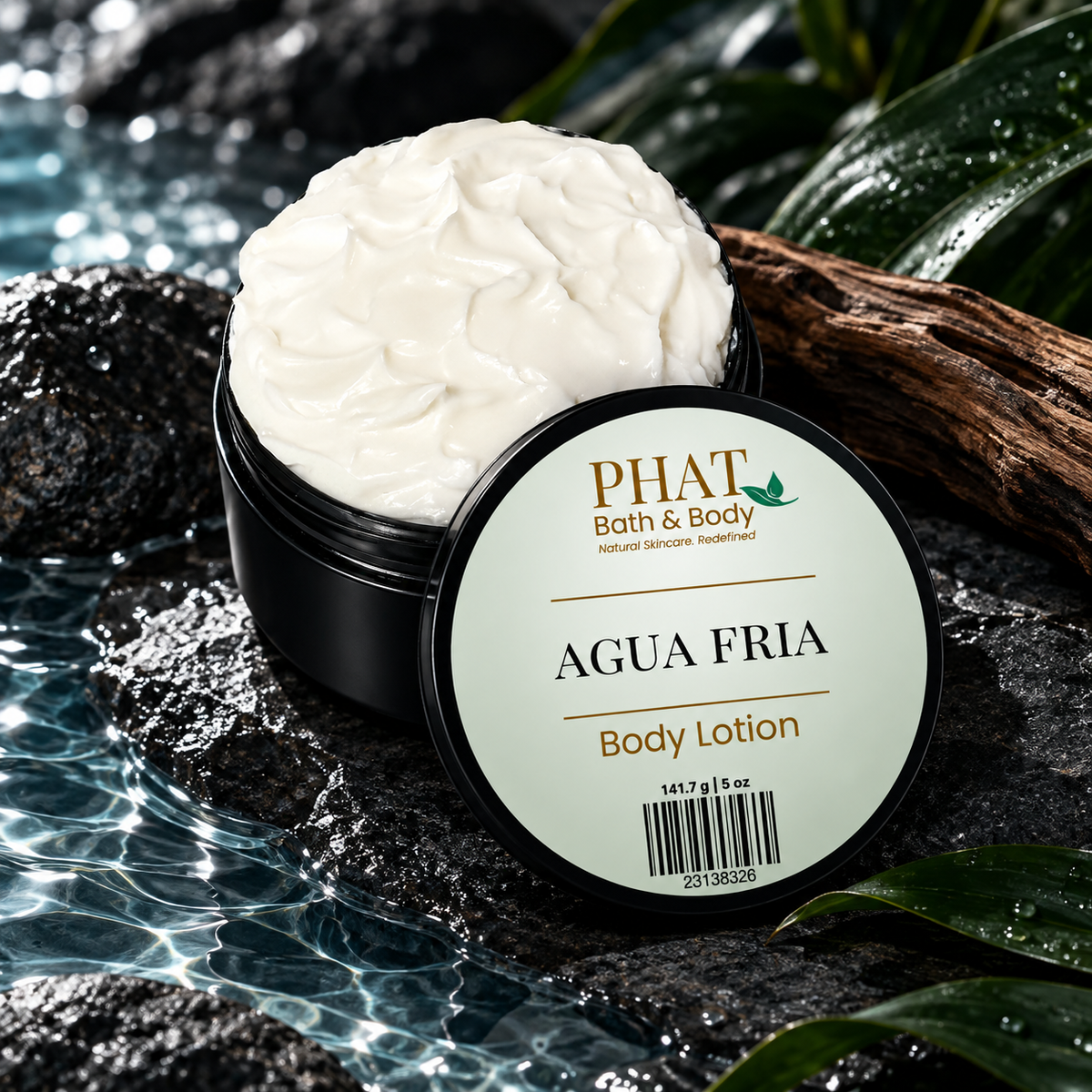 Open jar of Agua Fria Men’s Body Lotion with labeled lid displayed against cool water, dark stone, wood, and green foliage.