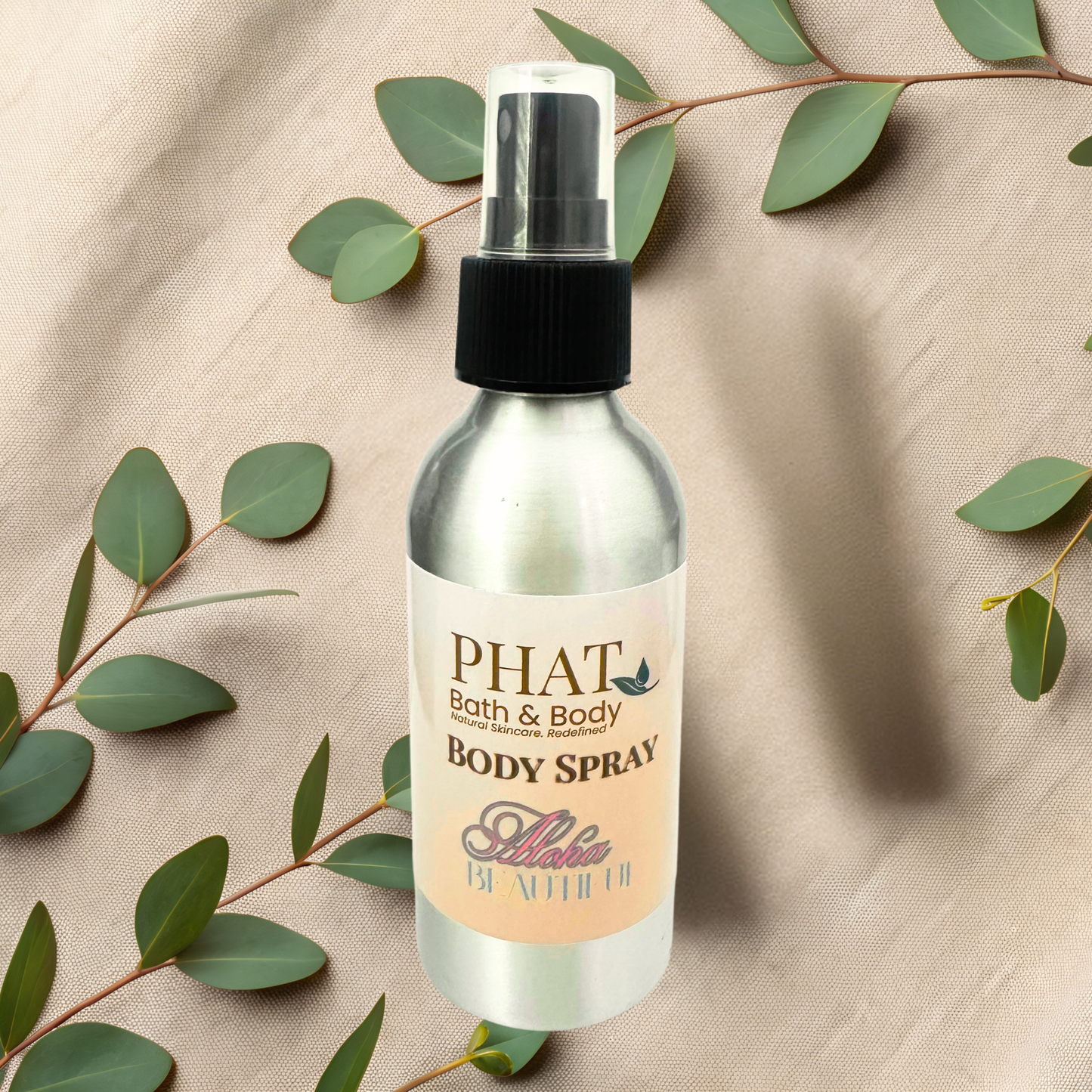 Body spray bottle labeled 'PHAT Bath & Body' on a beige fabric background with green leaves.
