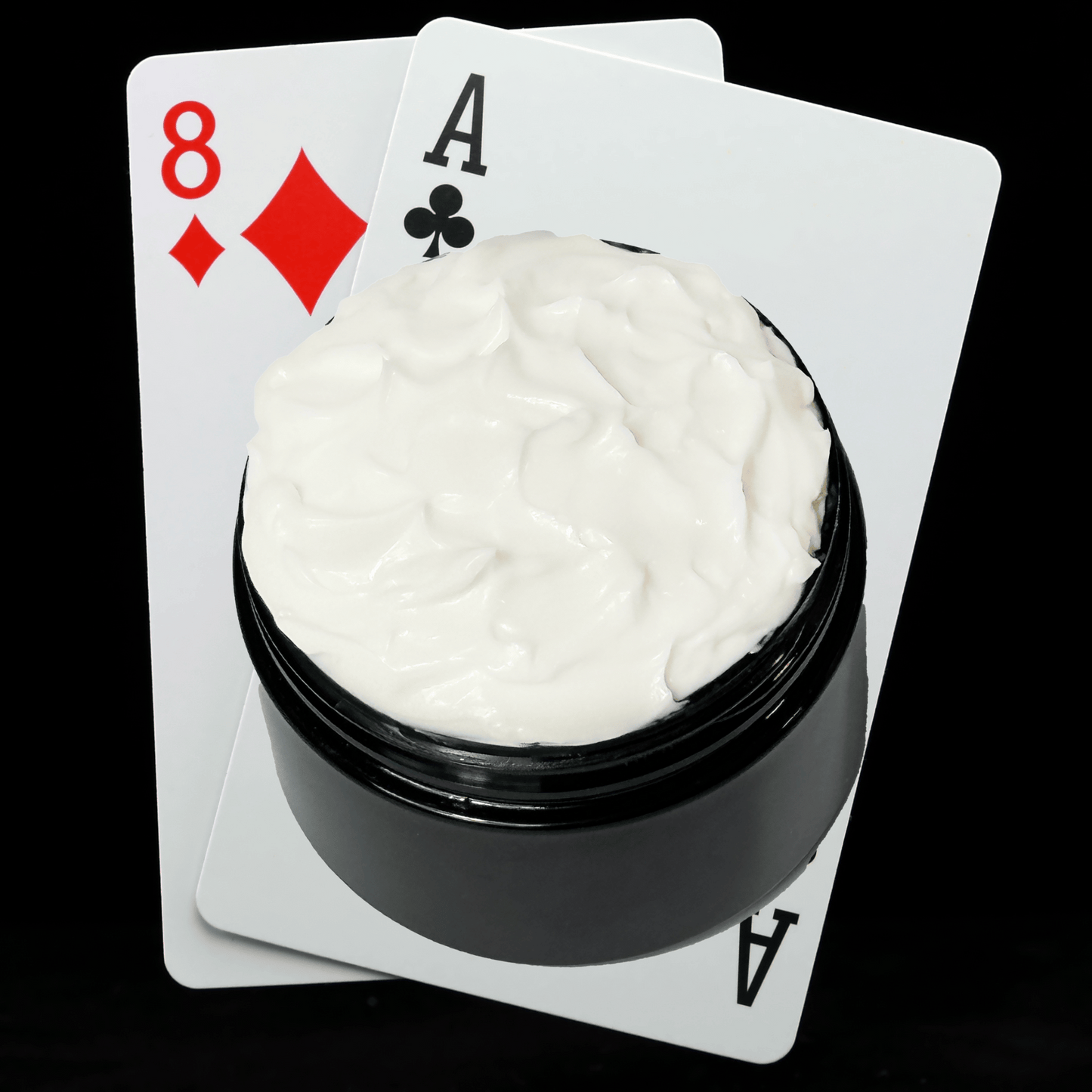 Black jar of cream with playing cards showing an Ace and an Eight on a white background