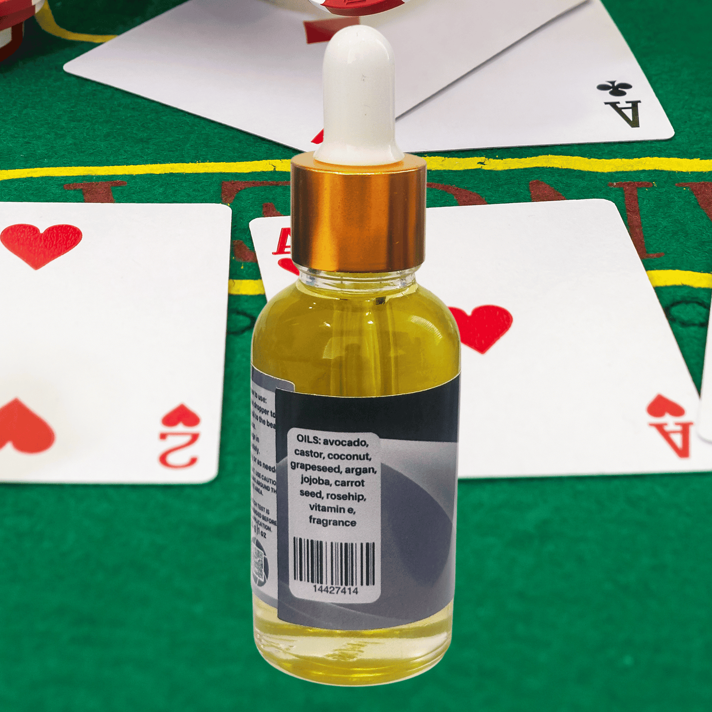 Bottle of beard oil with a dropper on a green surface with playing cards