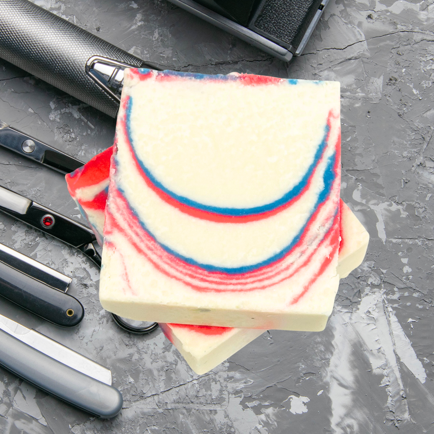 Marbled soap with red and blue stripes on a gray surface with razors.