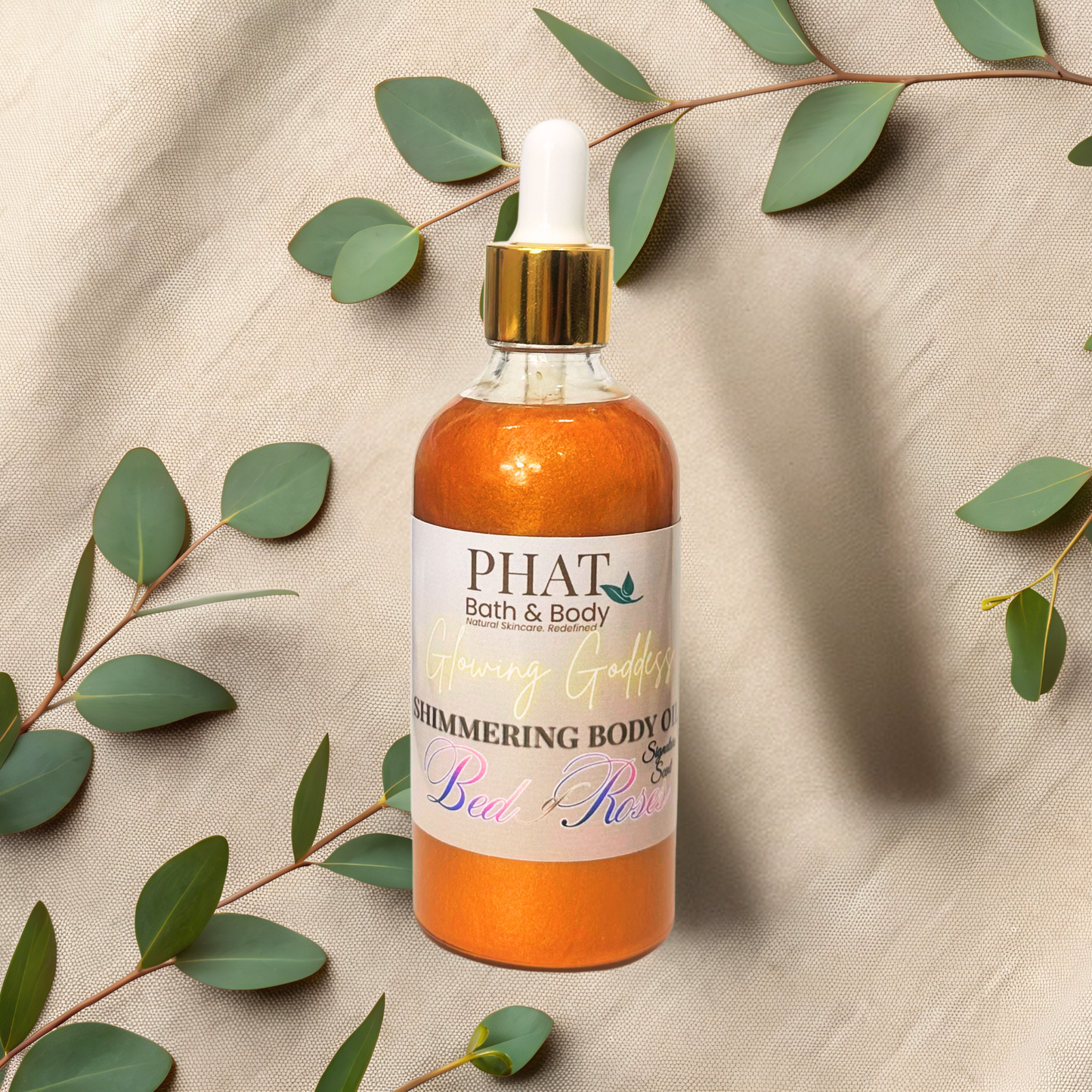 Bottle of 'PHAT Bath & Body' shimmering body oil with eucalyptus leaves on a beige fabric background