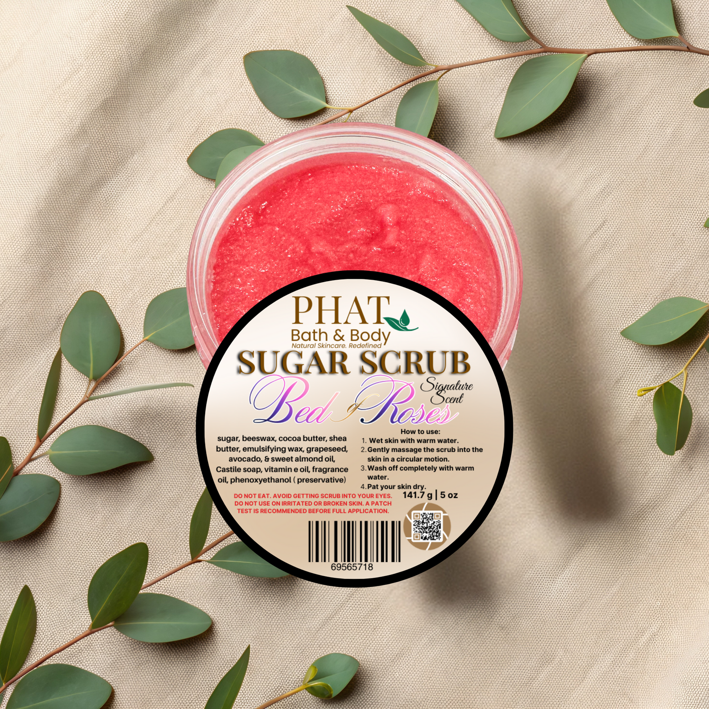 Jar of sugar scrub with a label on a beige fabric background with green leaves.
