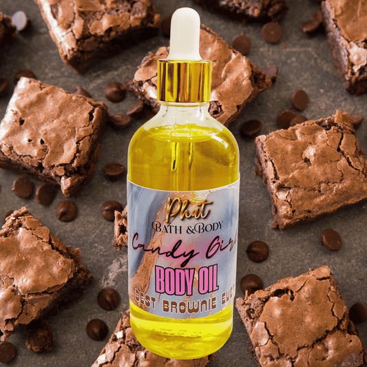 Body oil bottle labeled 'Candy Girl' surrounded by brownies and chocolate chips on a dark surface