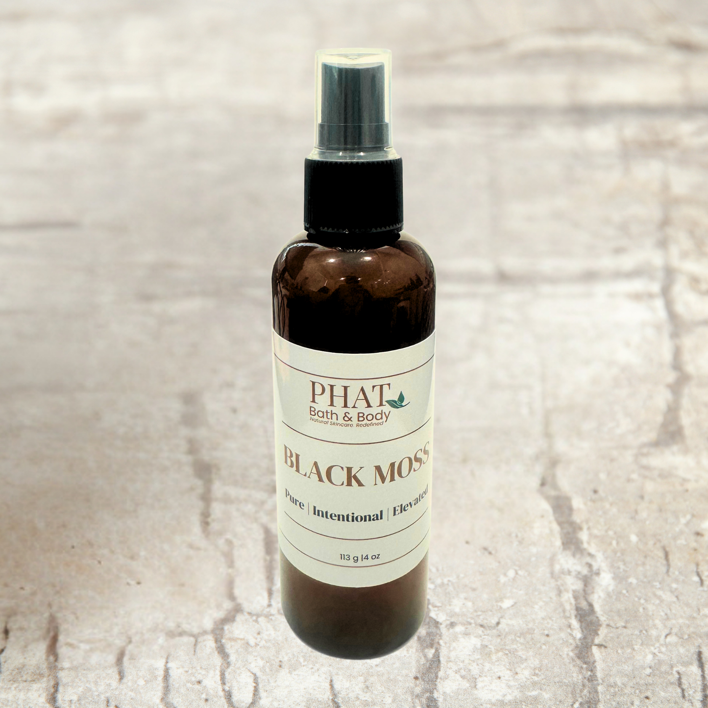 Brown spray bottle labeled 'PHAT Bath & Body Black Moss' on a textured beige background