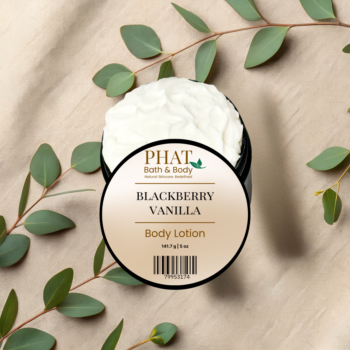 A round-labeled tub of PHAT Bath & Body Blackberry Vanilla Body Lotion filled with whipped white lotion, styled on a beige fabric background with eucalyptus leaves.