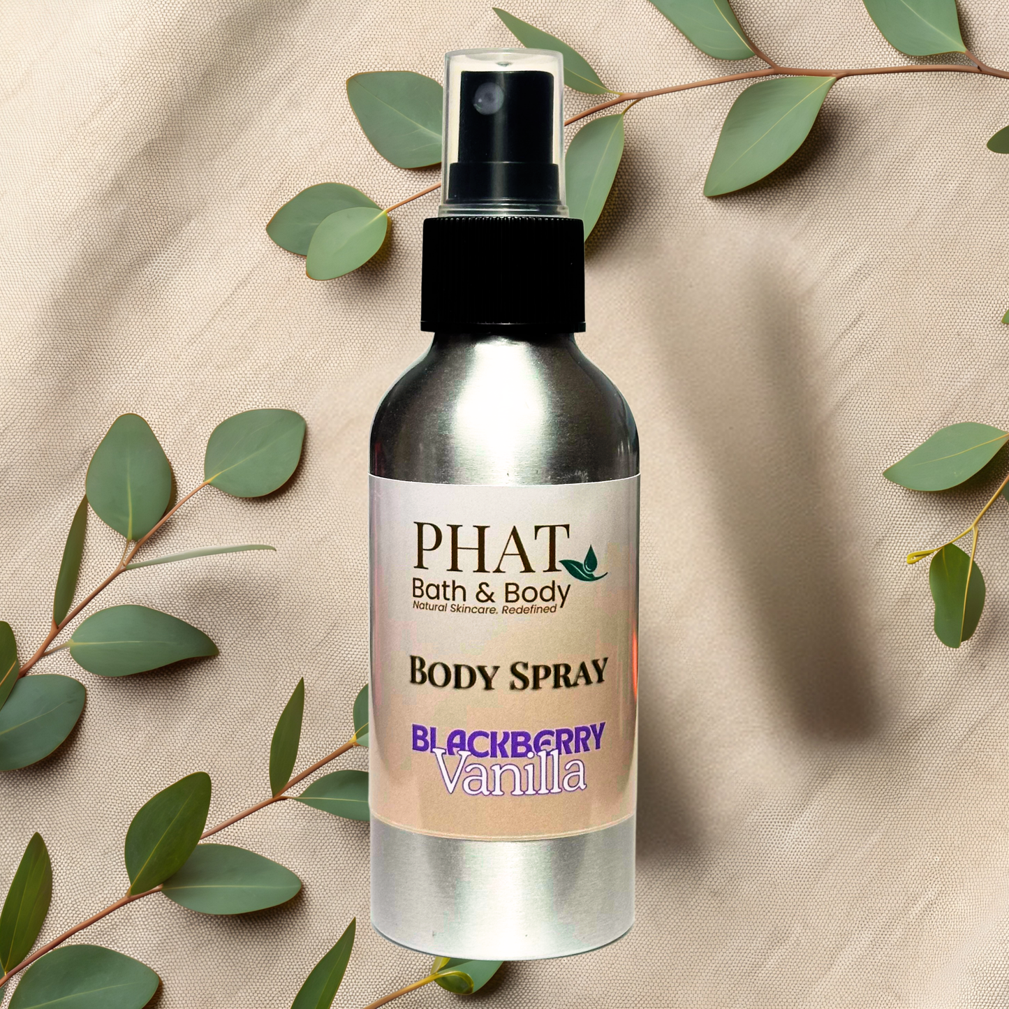 Body spray bottle labeled 'PHAT Bath & Body' with 'Blackberry Vanilla' scent on a beige fabric background with green leaves.