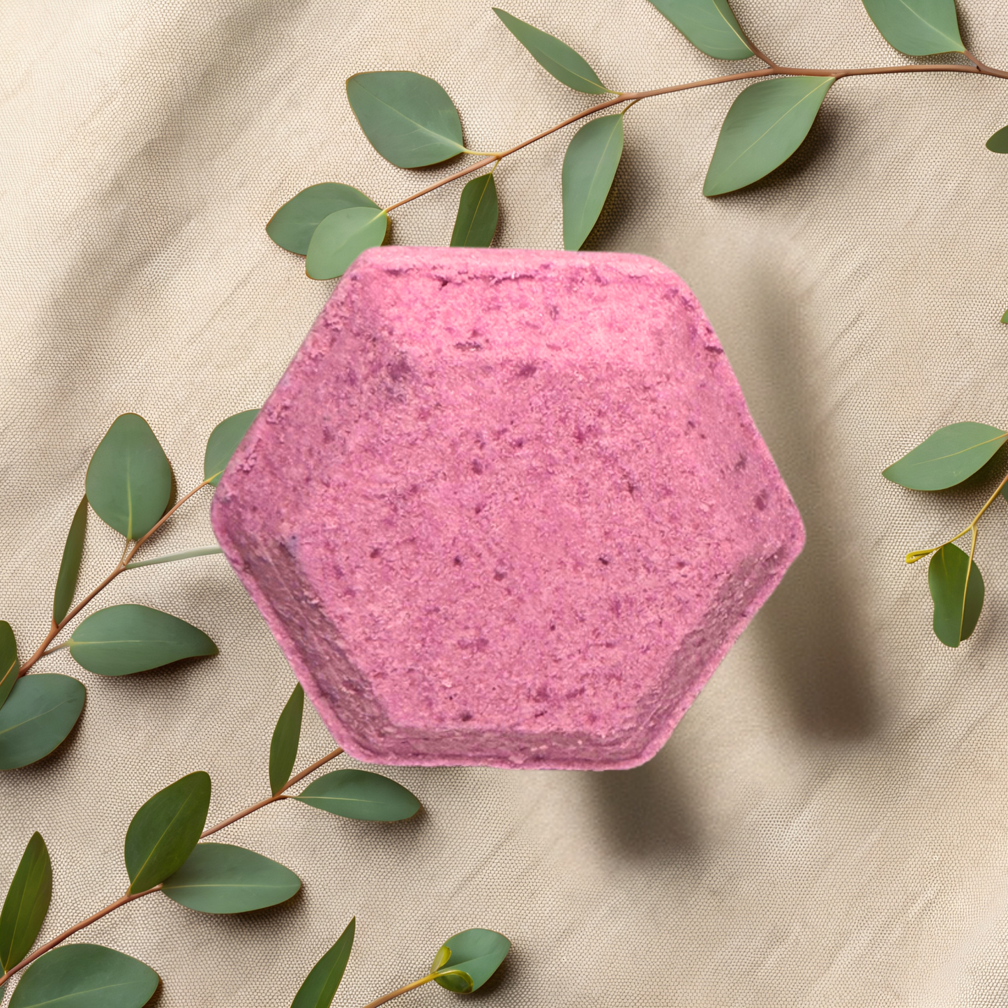 Hexagonal pink shower bomb with green leaves on a beige fabric background