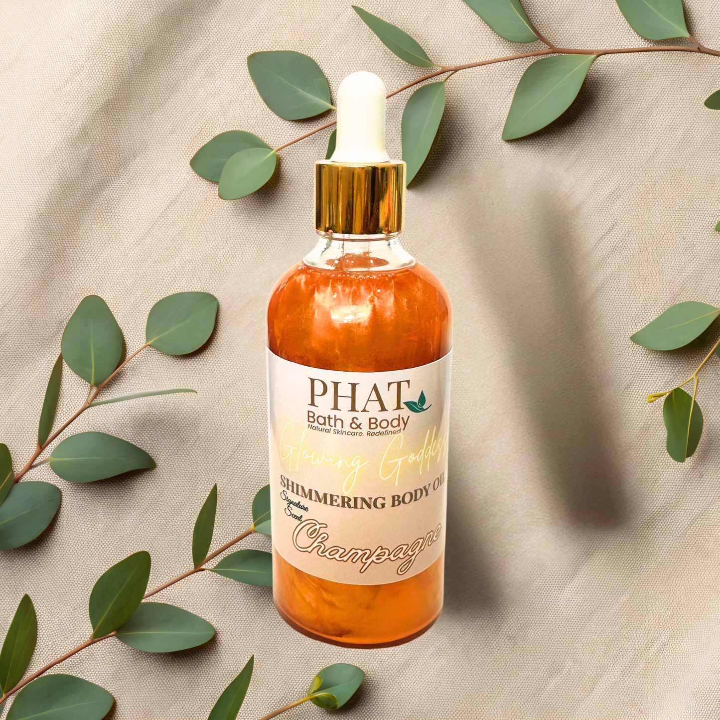 Bottle of 'PHAT Bath & Body' shimmering body oil with a dropper on a beige fabric background with green leaves.