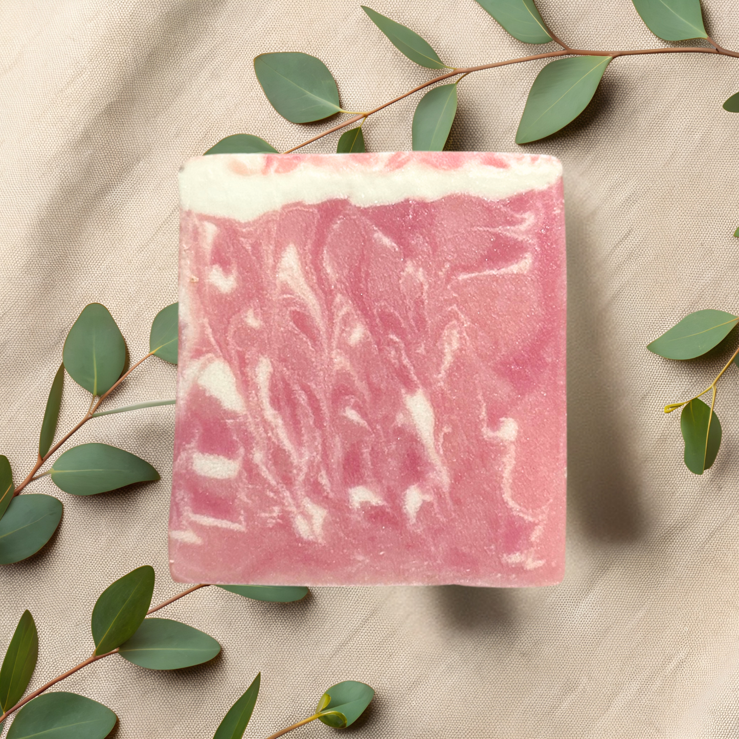 Pink soap bar with white swirls on a beige fabric background with green leaves.