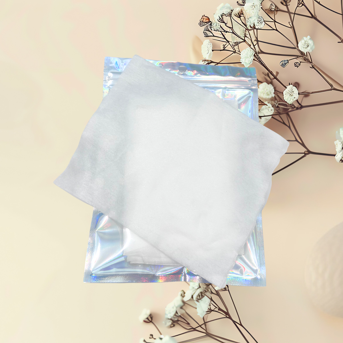 White cotton cloth in a clear plastic packaging on a beige background with white flowers.