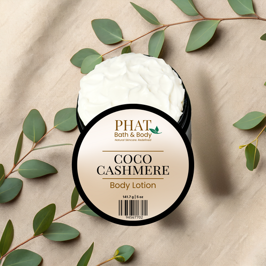 Body lotion jar labeled 'Coco Cashmere' from 'PHAT Bath & Body' on a beige fabric background with green leaves.