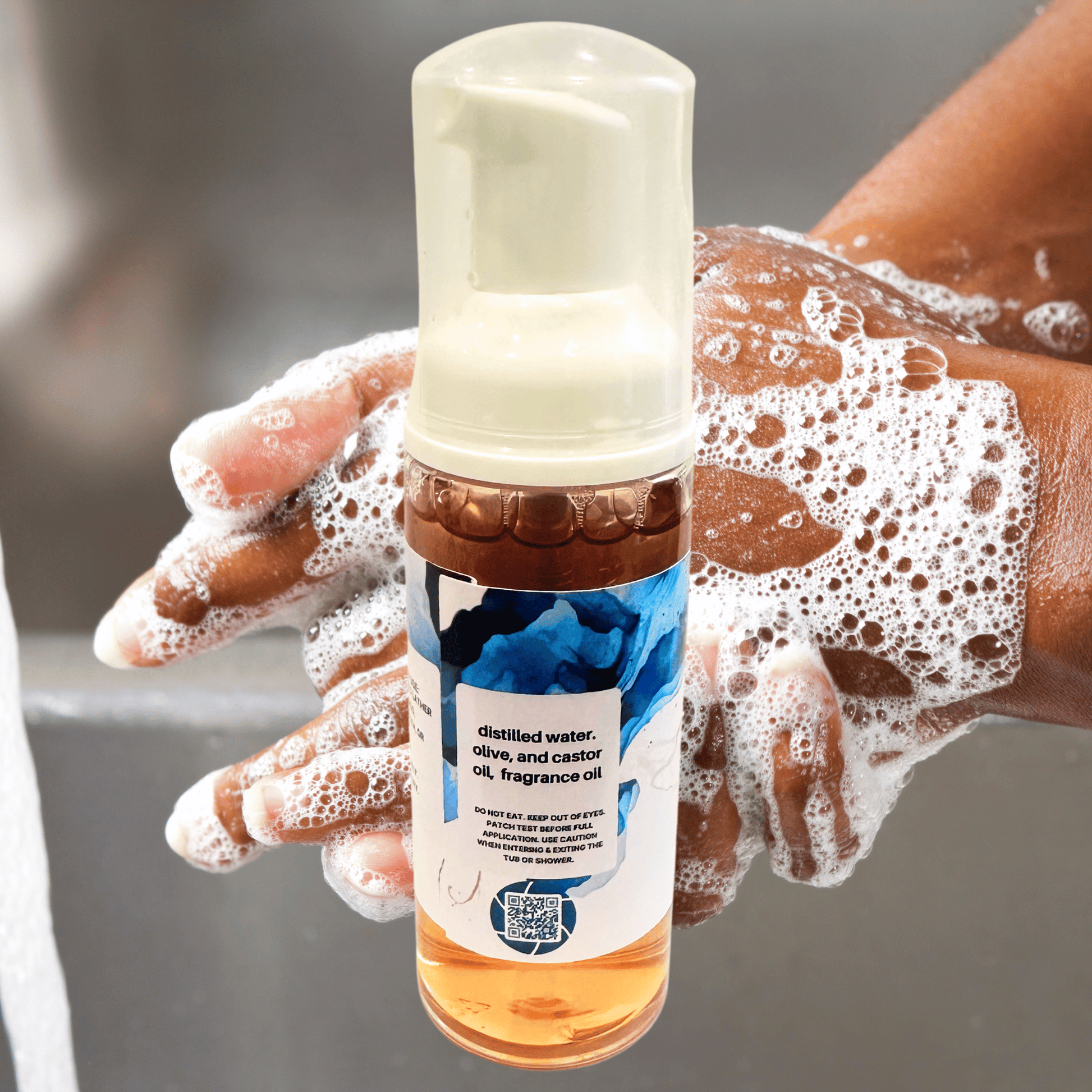 Bottle of foaming hand soap with a hand with soap suds, against a blurred background