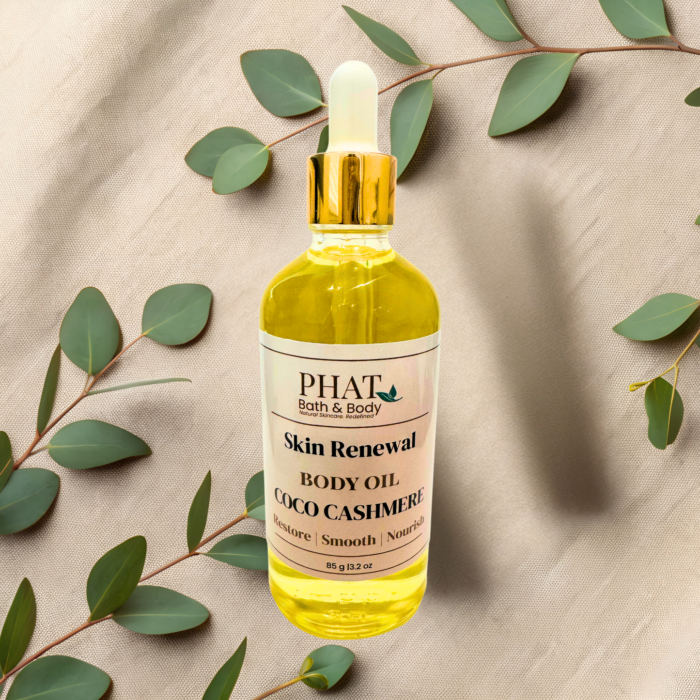 Bottle of PHAT Skin Renewal Body Oil with green leaves on a beige fabric background