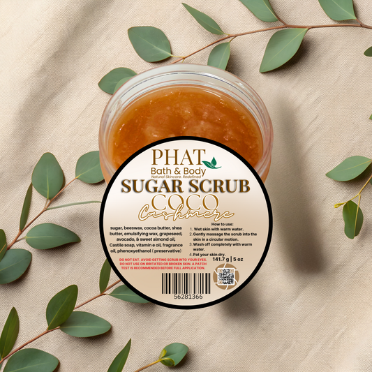 Jar of sugar scrub with a label on a beige fabric background with green leaves.