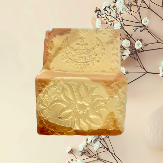 Two rectangular bars of soap with intricate designs on a light pink background with white flowers.