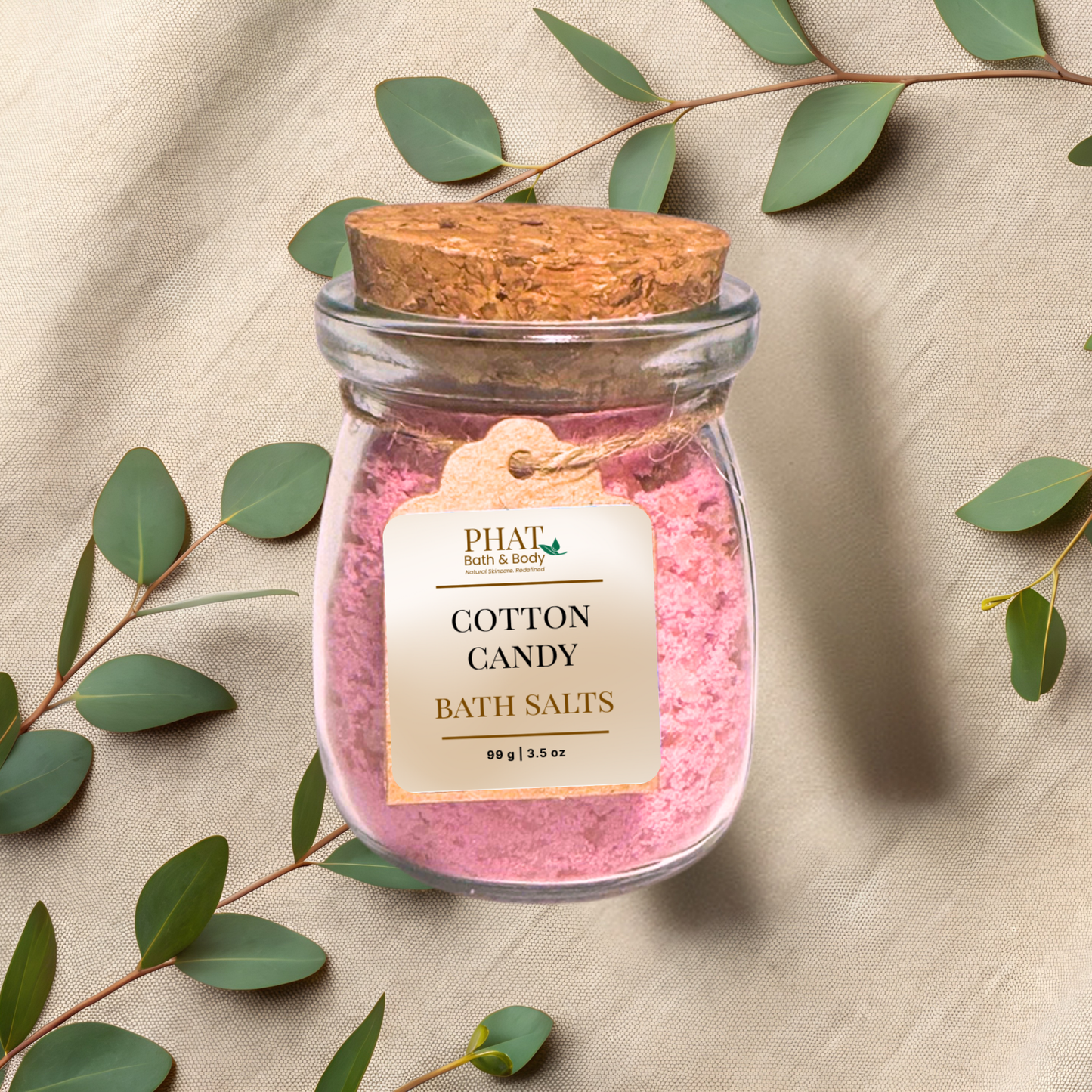 Jar of Cotton Candy Bath Salts with a cork lid on a beige fabric background with eucalyptus leaves.