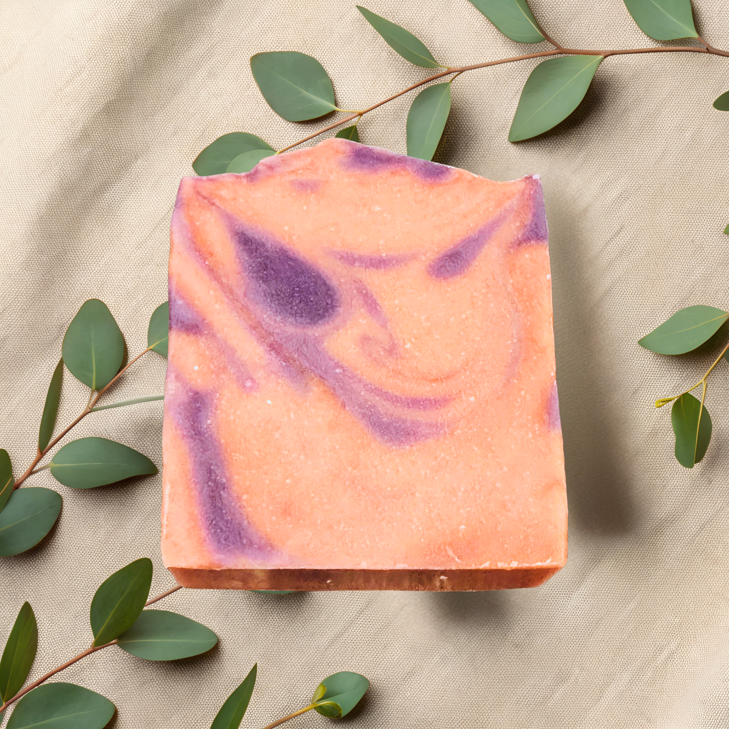 Swirled pink and purple soap bar on a beige fabric background with green leaves.