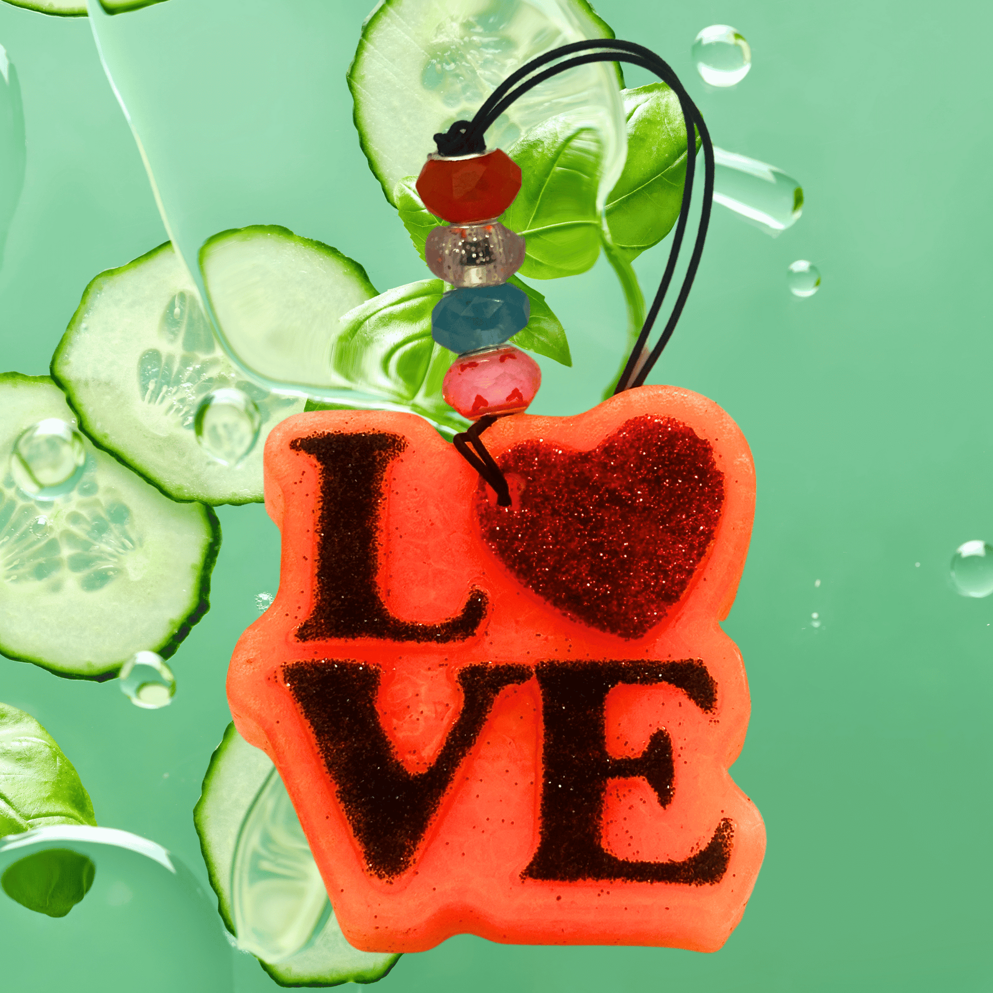 Red 'LOVE' charm with beads on a green background with cucumber slices