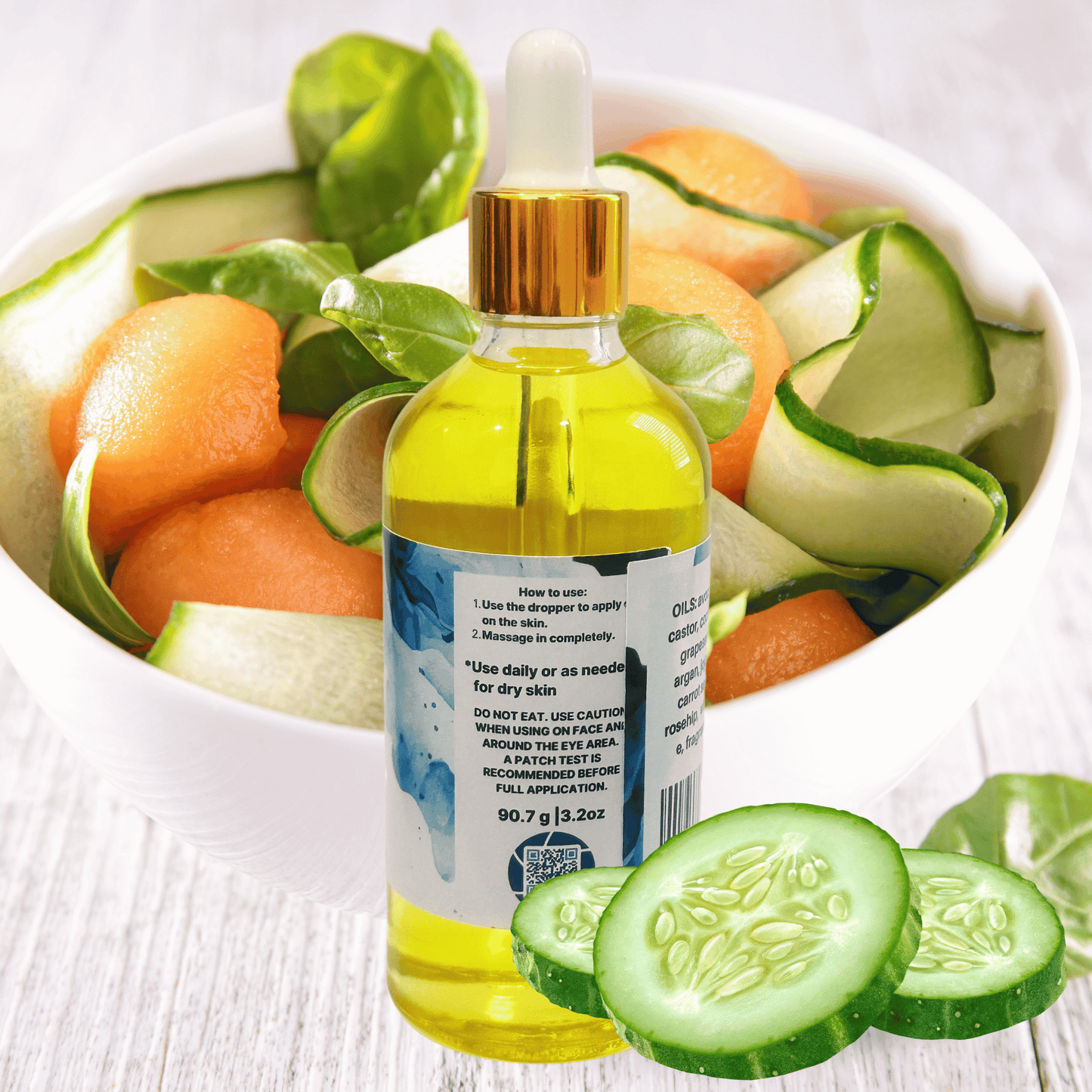 Bottle of body oil with a dropper surrounded by sliced cucumbers and melons on a white background