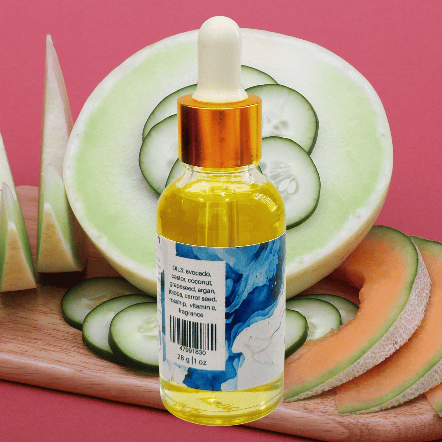 Bottle of oil with a dropper on a cutting board with sliced cucumbers, melon, and cantaloupe against a pink background