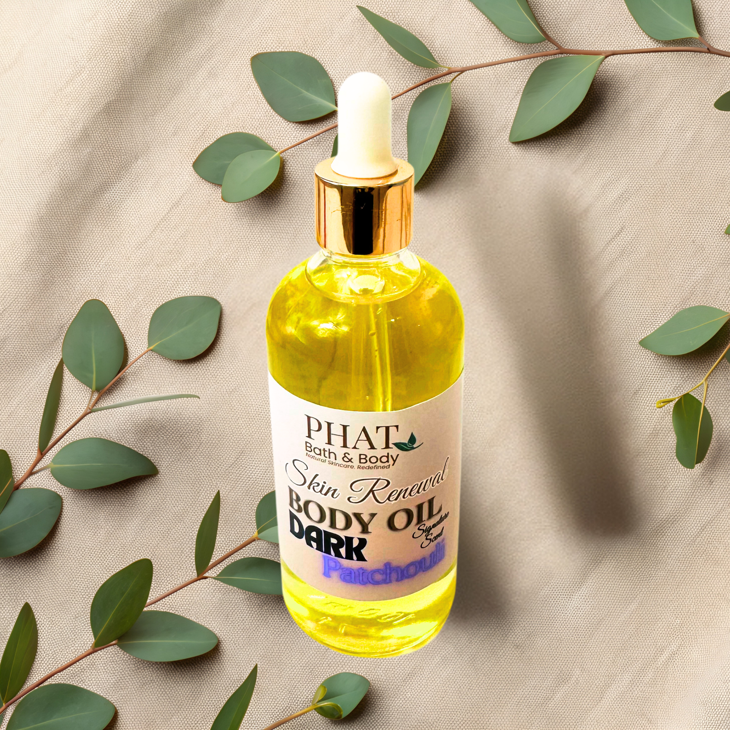 Bottle of PHAT Bath & Body Skin Renewal Body Oil Dark Patchouli on a beige fabric background with green leaves.