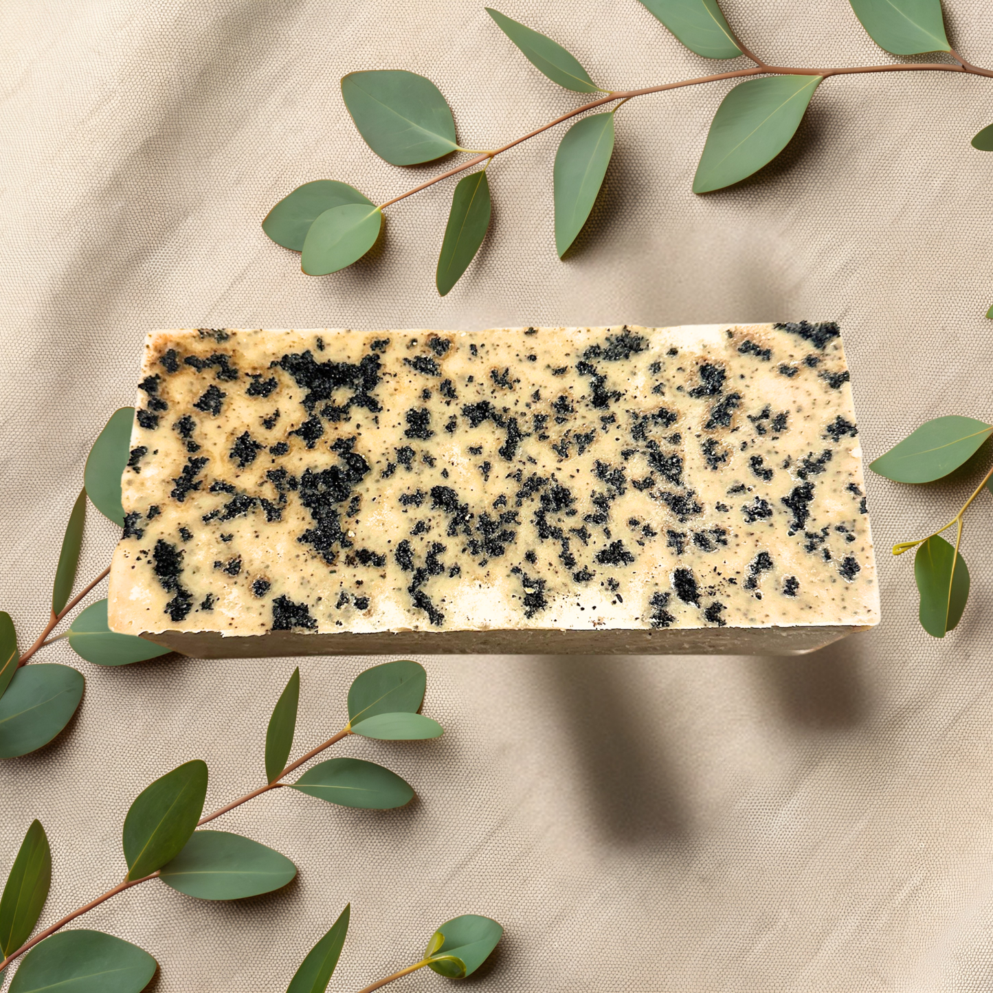Rectangular bar of soap with coffee specks on a beige fabric background with green leaves.