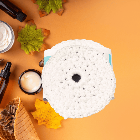 Round white crocheted scrubby on an orange background with leaves and small containers.