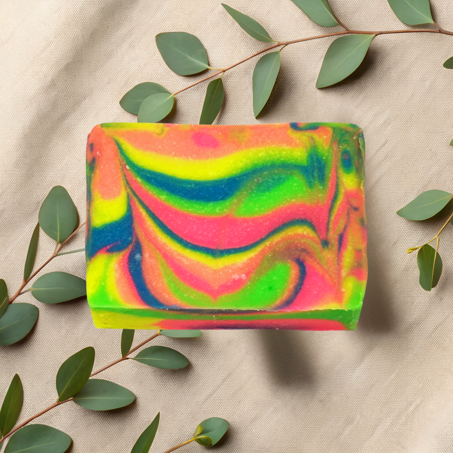 Colorful soap bar with a swirled pattern on a beige fabric background with green leaves.