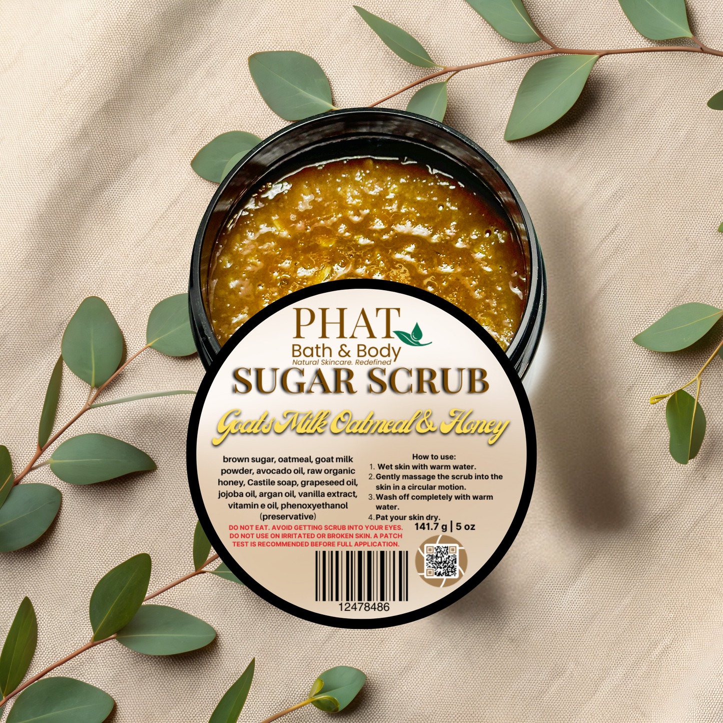 PHAT Bath & Body sugar scrub container with label on a beige fabric background with green leaves.