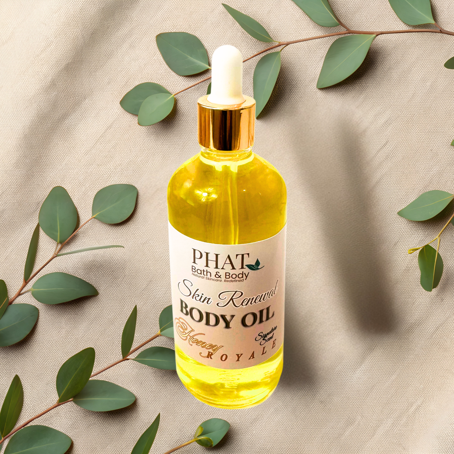 Bottle of PHAT Bath & Body body oil with a dropper on a beige fabric background with green leaves.