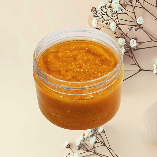 Jar of orange-colored scrub on a light background with white flowers.