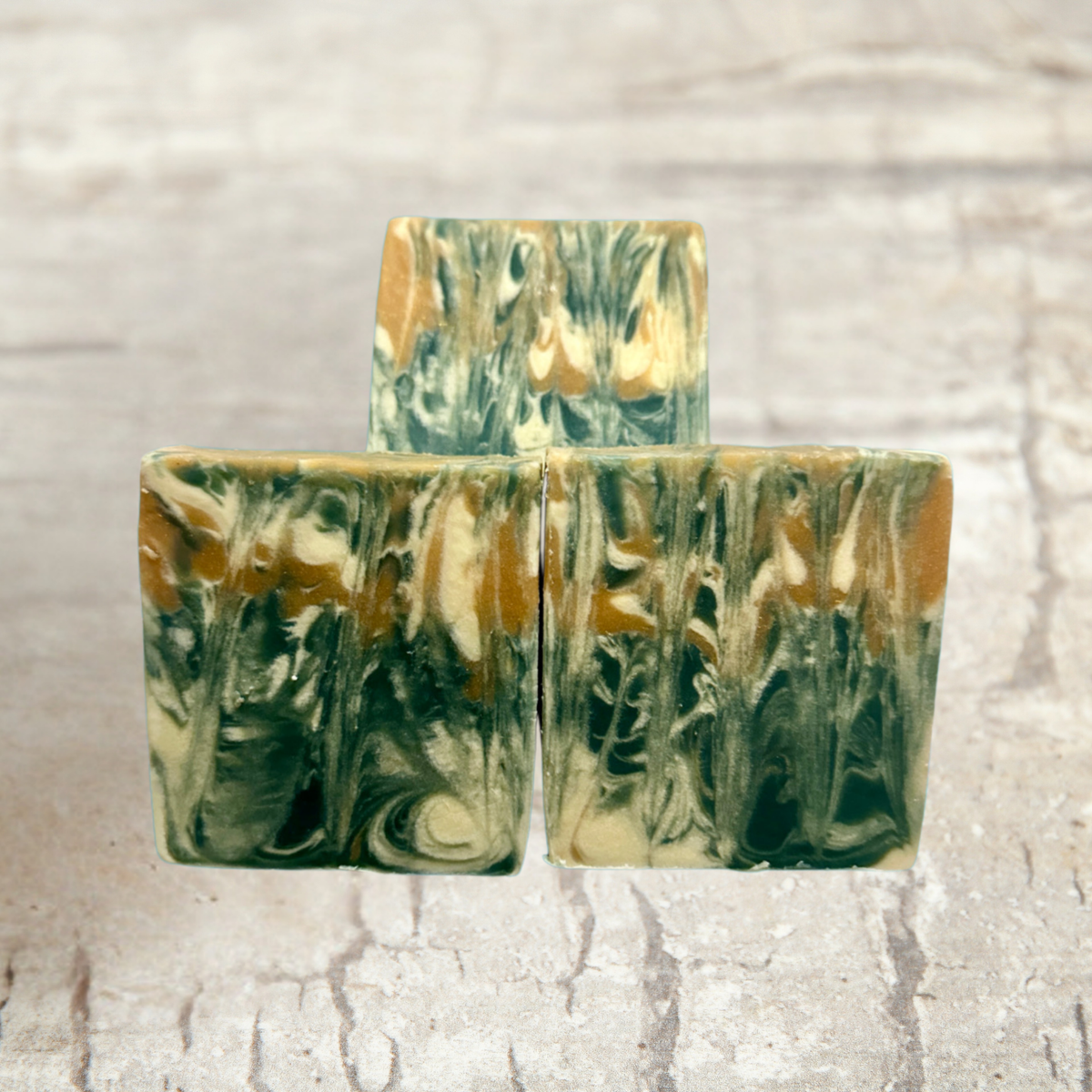 Three marbled soap bars with green and brown hues on a textured beige background