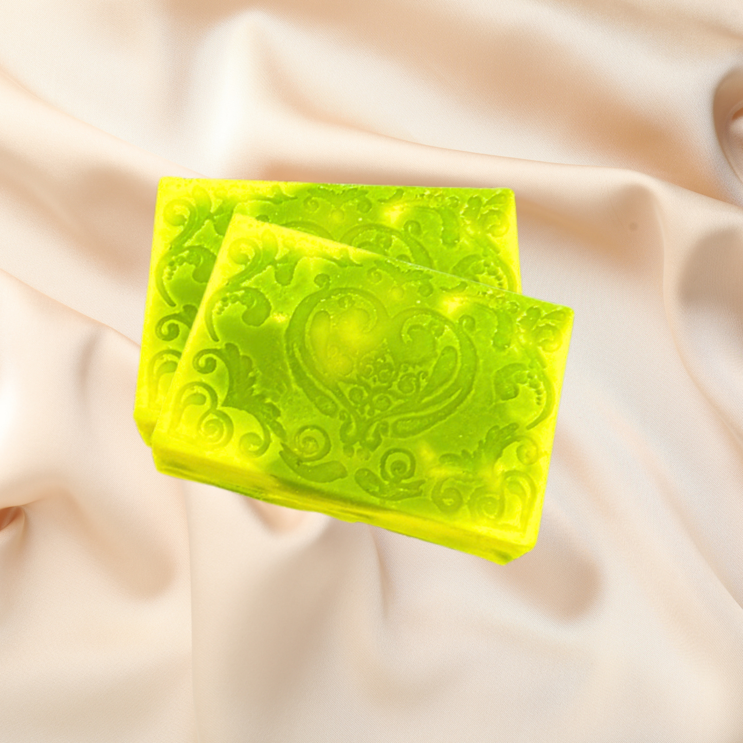 Two green soap bars with decorative patterns on a beige fabric background