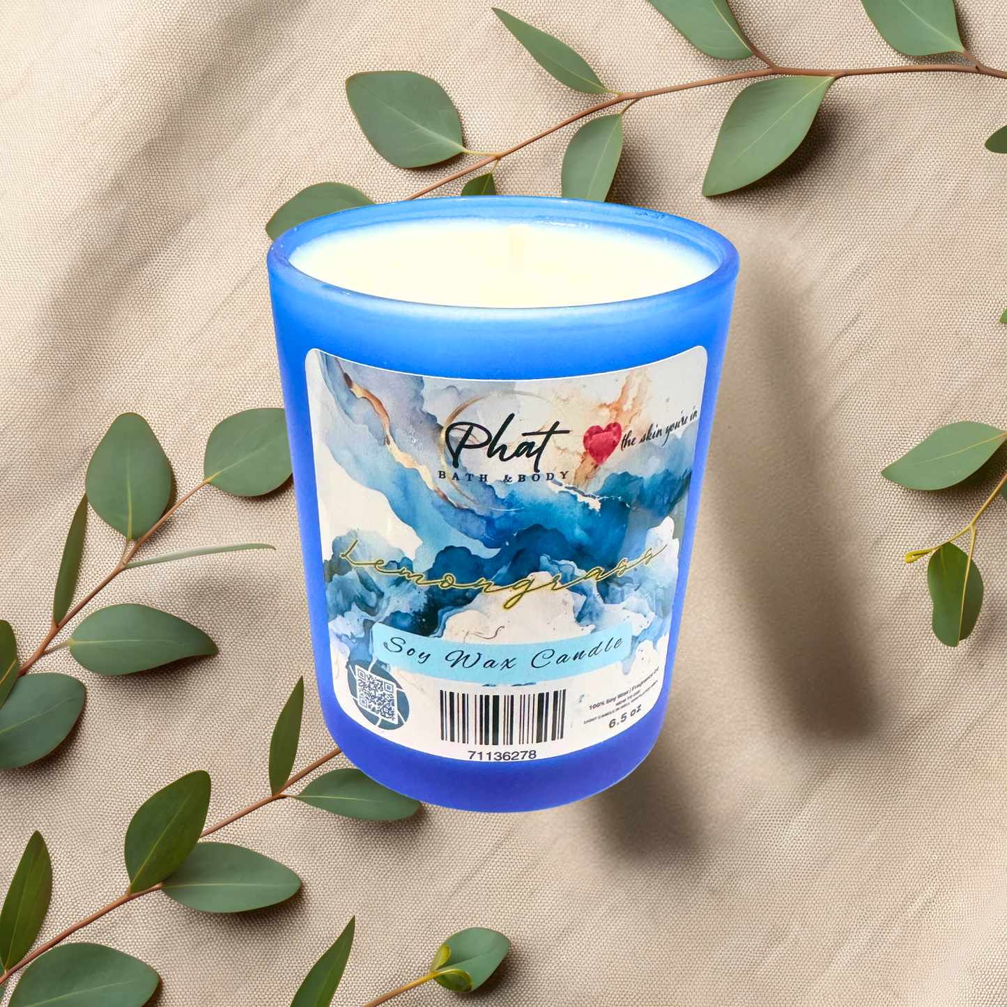 Blue candle with a decorative label on a beige fabric background with green leaves.