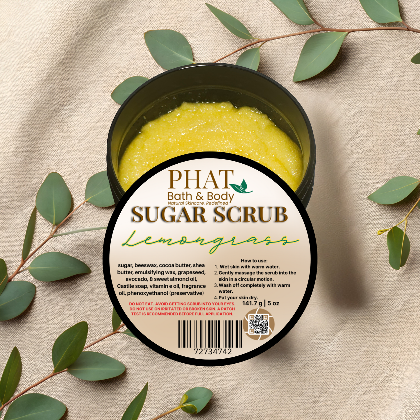 Container of Phat Bath & Body Lemongrass sugar scrub with green leaves on a beige fabric background