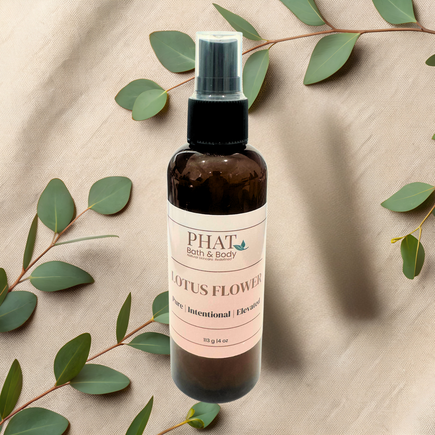 Bottle of PHAT Bath & Body Lotus Flower product on a beige fabric background with green leaves.