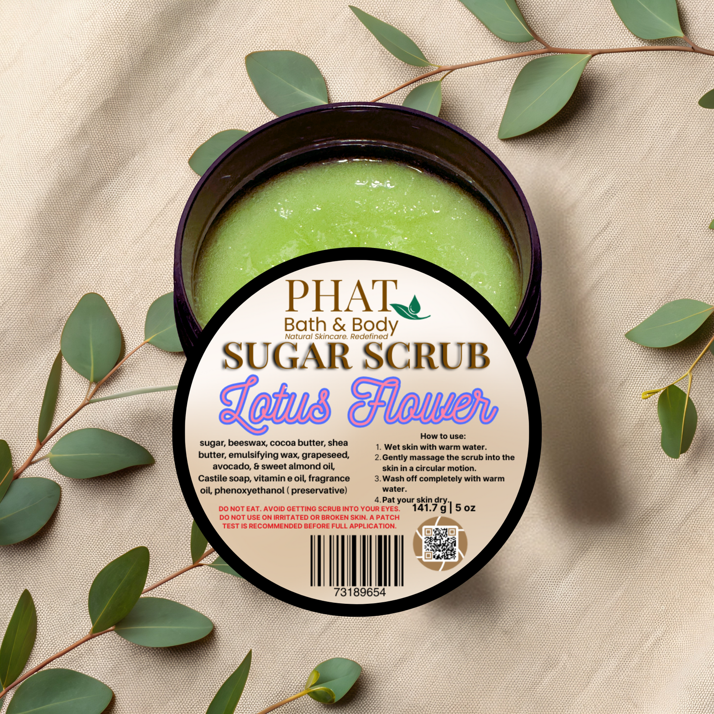 Green sugar scrub in a container with a 'Phat Bath & Body' label on a beige fabric background with green leaves.
