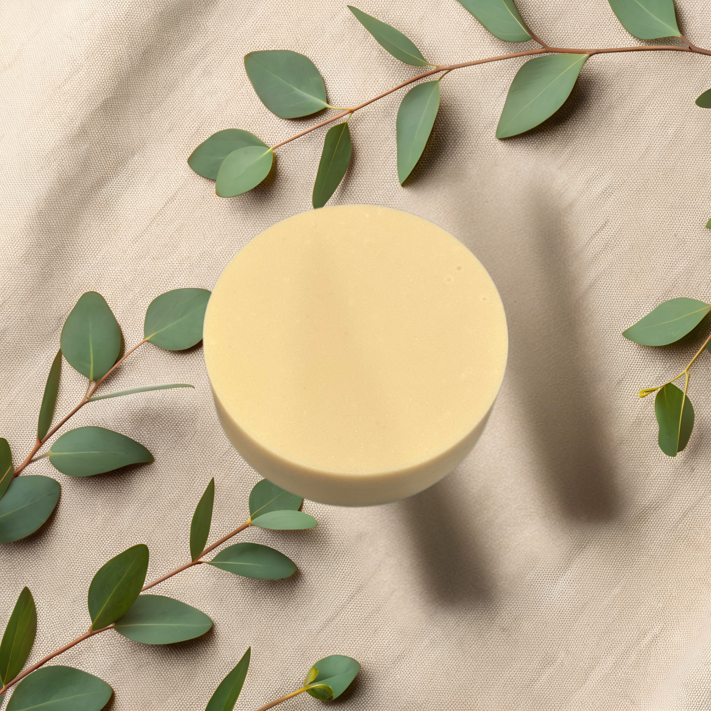 Round yellow soap bar on a beige fabric background with green leaves