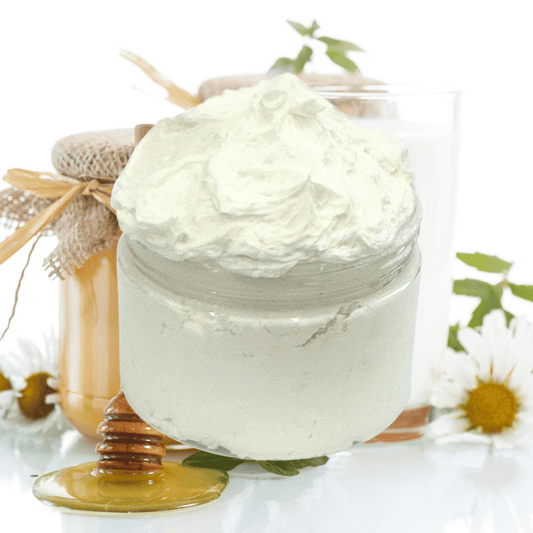 Jar of white body butter with a honey dipper and flowers on a white background