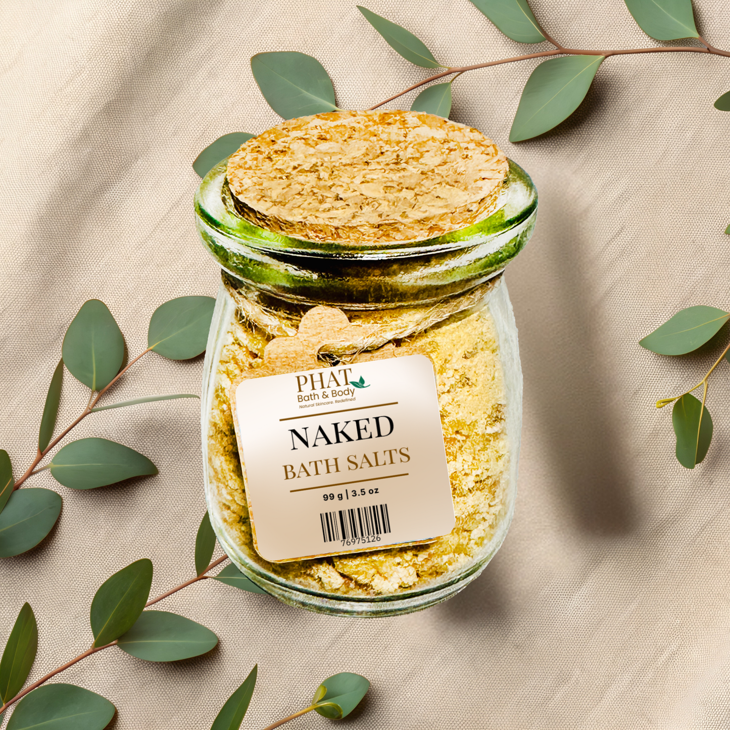 Glass jar of naked bath salts with a cork lid on a beige fabric background with eucalyptus leaves.