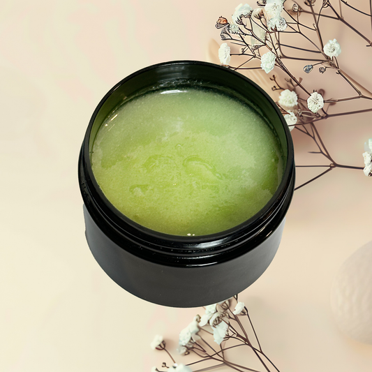 Black jar with green scrub on a light pink background with white flowers.