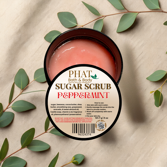 Jar of sugar scrub with peppermint scent on a beige fabric background with green leaves.