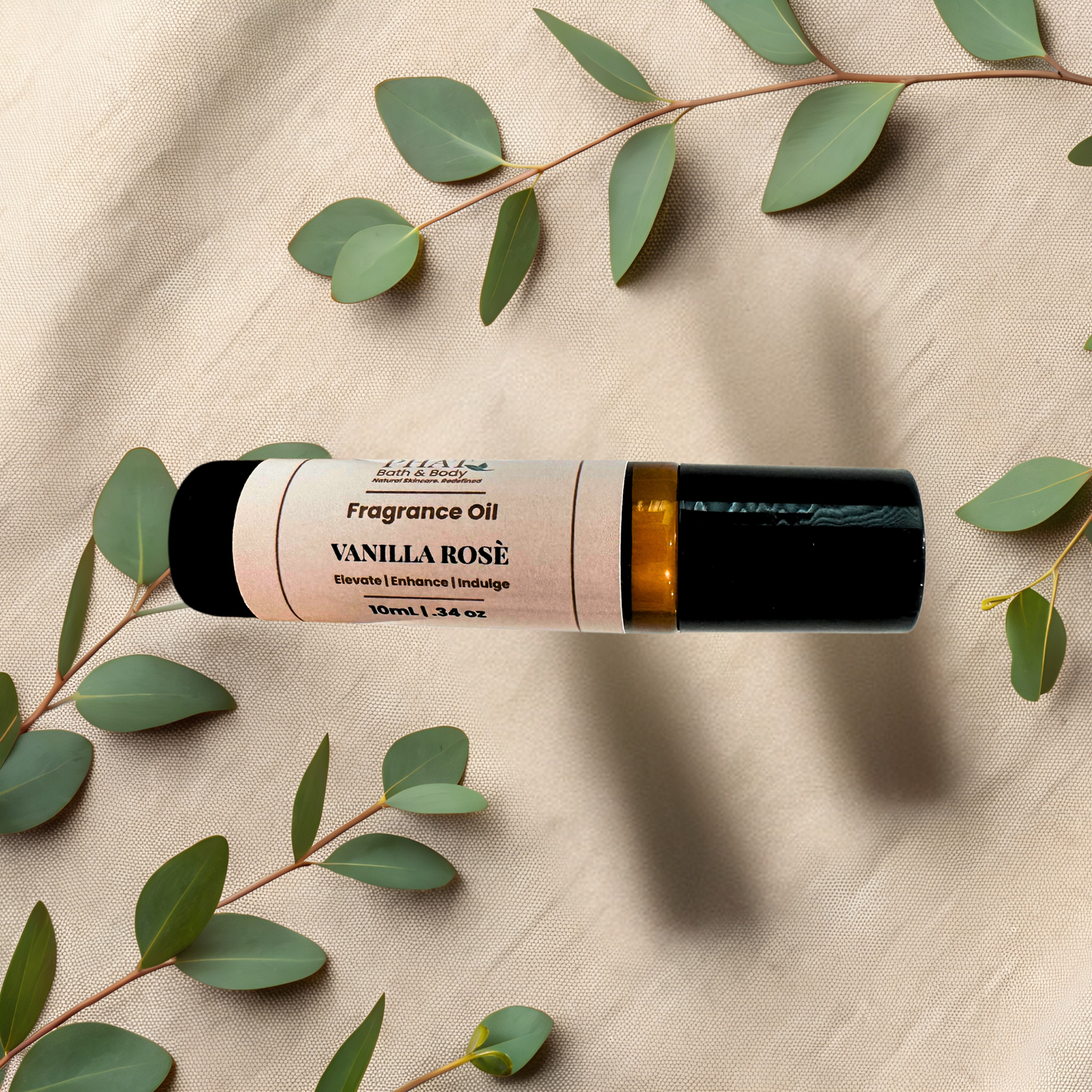 A roll-on bottle of Vanilla Rosé fragrance oil, styled on a beige fabric background with green eucalyptus leaves.