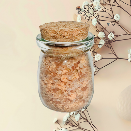 Glass jar with cork lid filled with pink Himalayan salt, placed on a light background with white flowers.