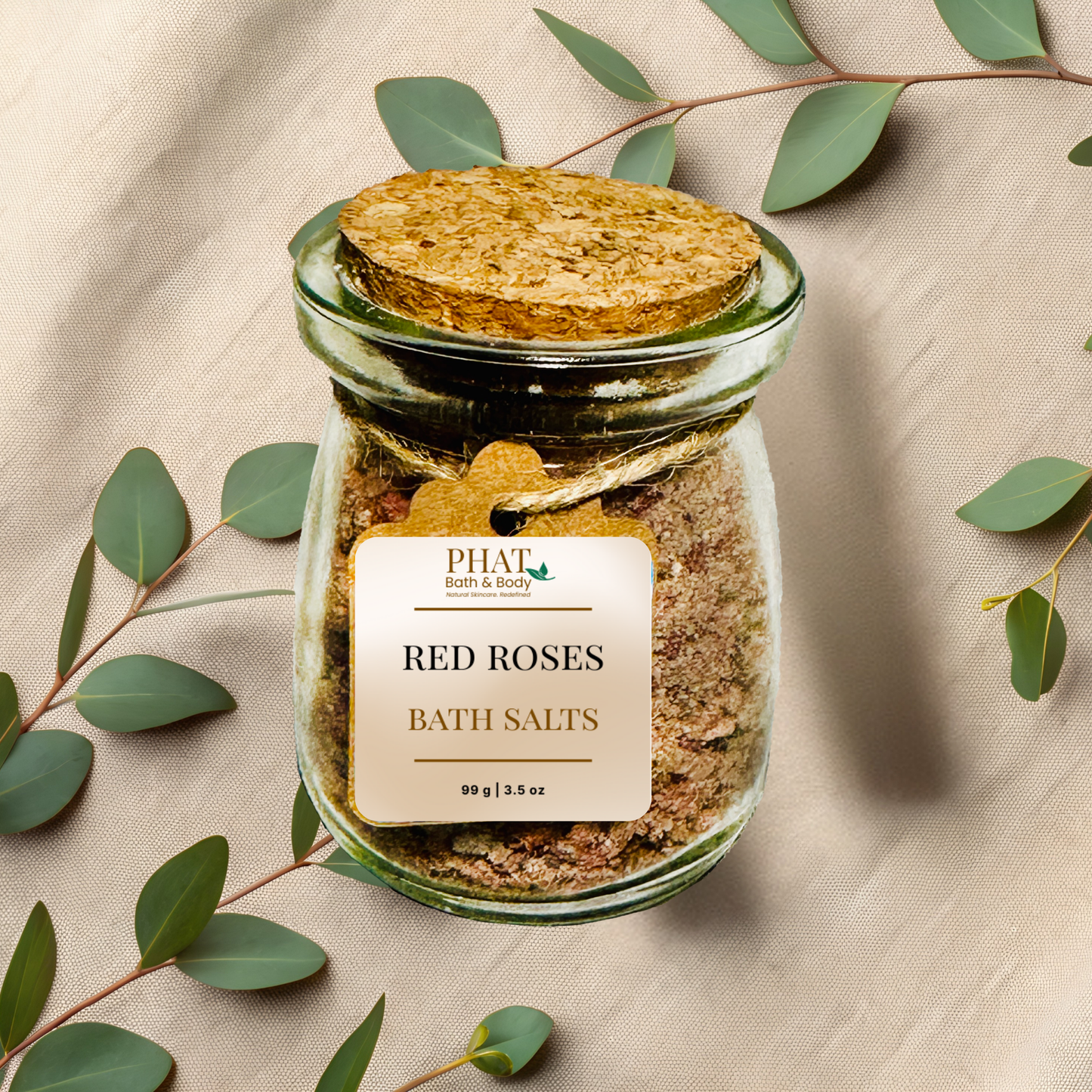 Jar of 'red roses' bath salts with a cork lid on a beige fabric background with eucalyptus leaves.