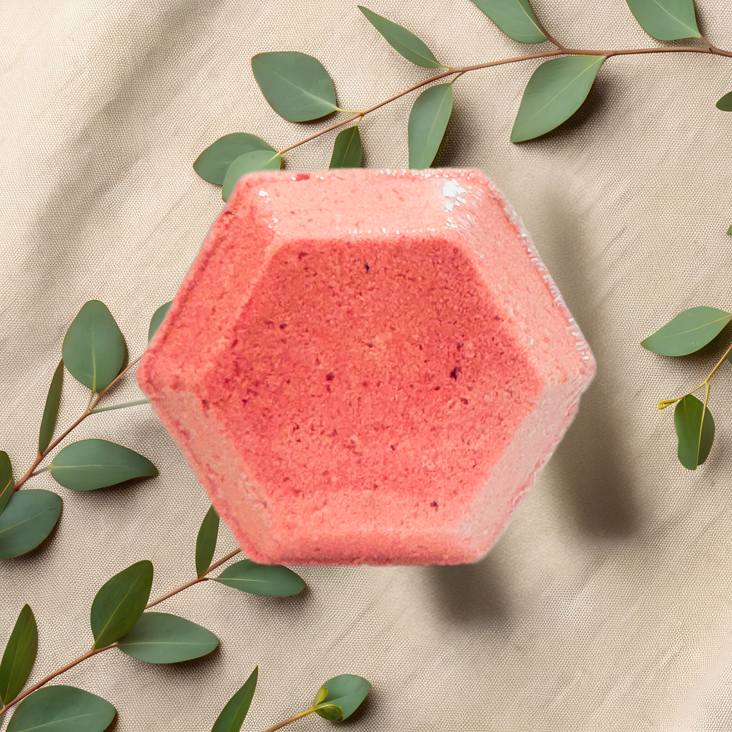 Hexagonal pink shower bomb on a beige fabric background with green leaves