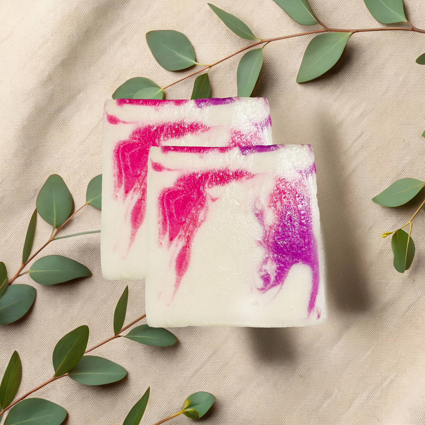 Two soap bars with pink and purple swirls on a beige fabric background with green leaves.
