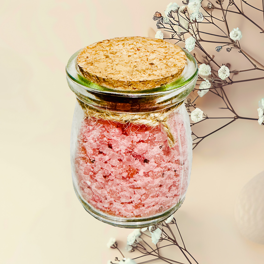 Glass jar with pink bath salts and cork lid on a neutral background